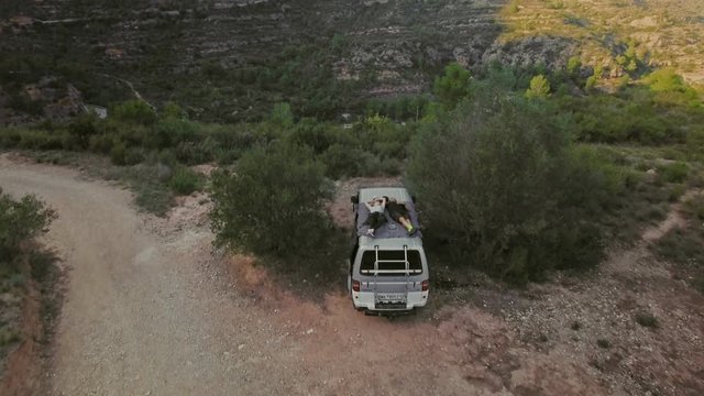 Epic drone footage of camera flying over happy married couple laying on top of their adventure van during hiking camping trip, enjoy relationship together. concept nomad lifestyle