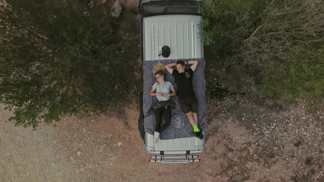 Top view with zoom out on romantic couple on date, laying on roof of car or van, watch stars or sky in natural national park, secluded camping site in wilderness, concept relationship goals or