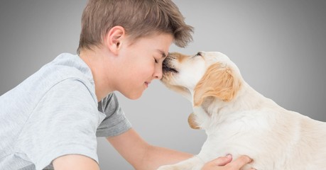 Obraz na płótnie Canvas Boy against grey background with friendly dog licking his face
