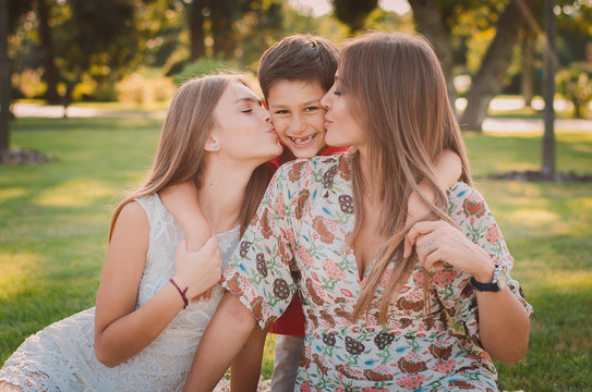 Happy mother, son and daughter in the park. Mom and sister kiss their son. Happy family concept.