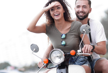 Beautiful young couple is smiling while riding a scooter