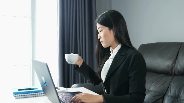 4k of Beautiful young business woman drinking coffee and working on laptop computer in office