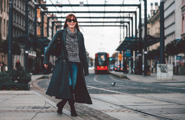 Trendy fashion woman in coat walking on the street, city scene