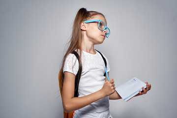 girl schoolgirl in blue glasses on a gray background reflected on a note in her notebook