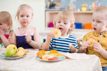 funny children group eating fruits in kindergarten dinning room