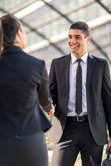 Two smiling young business people shaking hands while standing outdoors