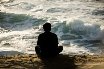 Fototapeta premium Silhouette of man sitting on sunset cliffs in San Diego california watching ocean