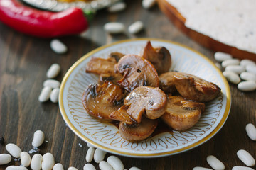 Roasted mushrooms on white ceramic plate on kitchen table.