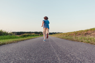 Boy running away on a long road in the fields