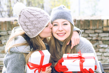 Teenagers sisters exchanging present and kissing outdoors at winter season - Best female friends hugging at park holding gift looking at camera and smiling - Concept of friendship holidays and love