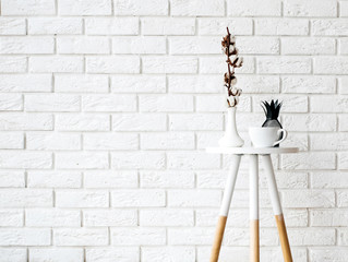 Small coffee table with cup and decor on the white brick wall background.
