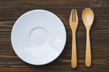 White plate and wooden spoon and fork place on wooden table