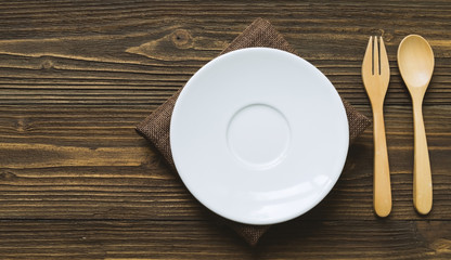 White plate and wooden spoon and fork place on wooden table