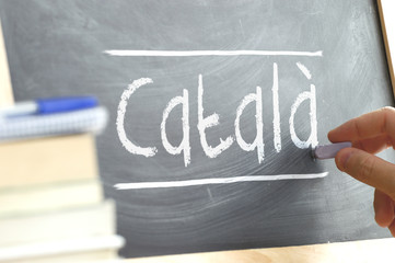 Hand writing on a blackboard in a language class with the word CATALAN wrote on. Some books and...