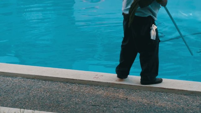 Man in working form to clean the bottom of a blue swimming pool