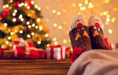 Detail of woman legs with knitted socks, Christmas tree with gifts