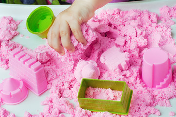 Child's hand playing with kinetic sand on the white table