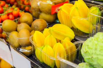 Variety of exotic fruits in plastic trays in the supermarket, vegetable shop, farmer marketplace. Organic, healthy, vegetarian diet food concept. Selective focus