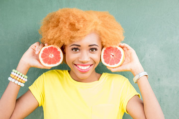 Portrait of a beautiful african woman with grapefruit slices on the green wall background