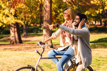 Obraz premium Happy young couple having fun riding a bicycle on sunny autumn day in the park. 