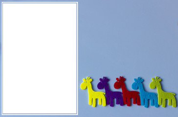 Fototapeta premium Baby birthday invitation concept. Giraffes small toys on blue background with empty white paper.