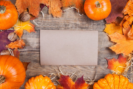 Thanksgiving Day concept -  border or frame with orange pumpkins and colourful leaves on wooden background with blank tag paper for text