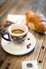 Espresso con cornetto appoggiato su tovagliolo con disegnato un flamingo e chicchi di caffè sparsi sul bancone in legno