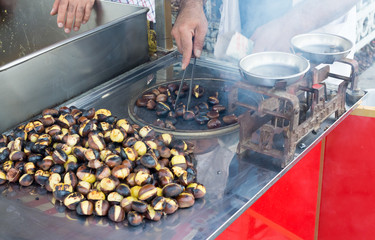 Man preparing roasted chestnuts, cooking outdoors.