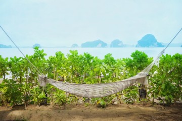 Hanging hammock or cradle made by woven rope on the beach with the background of the seascape, Relaxing on the beach during the vacation by lay down on the hammock and enjoy your time with nature