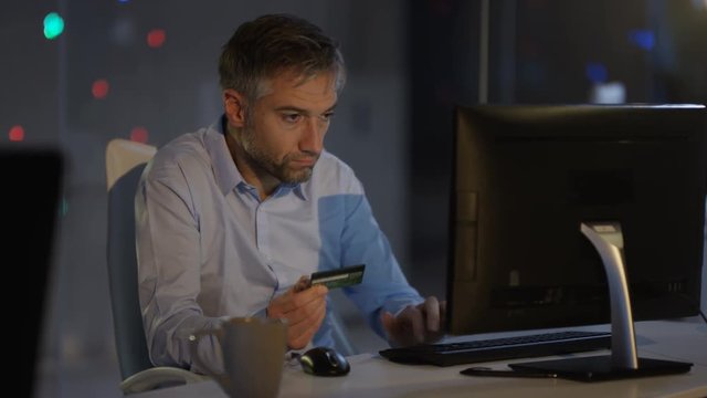  Businessman working late in the office, using credit card to shop online