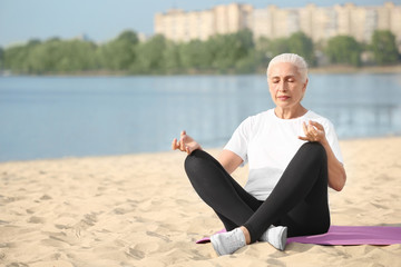 Fototapeta na wymiar Senior woman practicing yoga near river