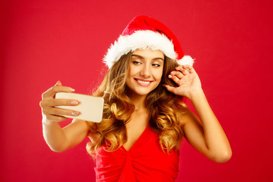 Young happy Santa woman in red dress taking her selfie over red background