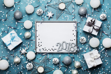 New year 2018 party background. Silver frame with christmas decoration, gift box, confetti and sequins on vintage blue table top view. Flat lay. Festive mockup or invitation.