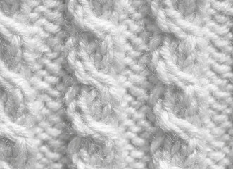 Texture of a knitted cloth with patterns of white color. Background of woolen threads handmade.