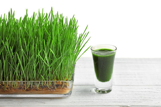 Composition with shot of healthy wheat grass juice on white wooden table