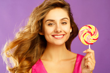 Portrait of a happy pretty girl holding sweet candy over violet background