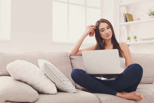 Young girl with laptop sitting on beige couch
