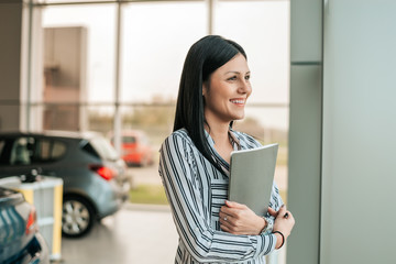 Young car saleswoman holding clipboard in showroom.