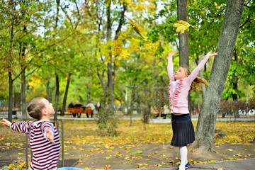 The boy gives the girl flowers from the autumn leaves to the bench in the park