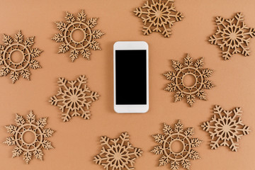 Wood craft snowflakes, bows, mobile phone with copy space on screen on beige background