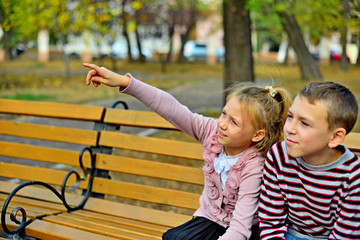 Obraz na płótnie Canvas Brother and sister cuddling and sitting on a bench in a park on autumn day. Little girl and boy hugging