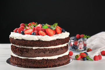 Delicious chocolate cake with berries on table against black background