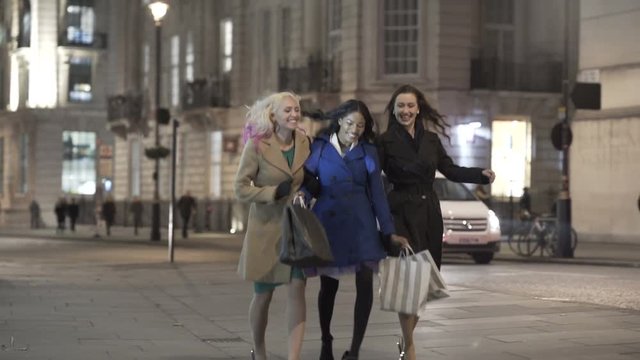  Happy female friends with shopping bags walking through the city at night