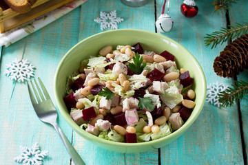 Homemade appetizer on a festive Christmas table. Salad with beets, Peking cabbage, meat and beans. Top view.