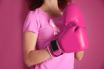 Young woman in pink t-shirt and boxing gloves on color background. Breast cancer awareness concept