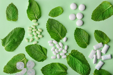 Different hard candies, chewing gum and mint leaves on color background