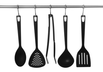 Set of cooking utensils hanging on rack, isolated on white