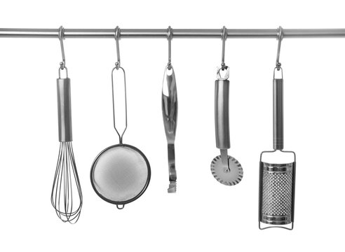 Set of cooking utensils hanging on rack, isolated on white