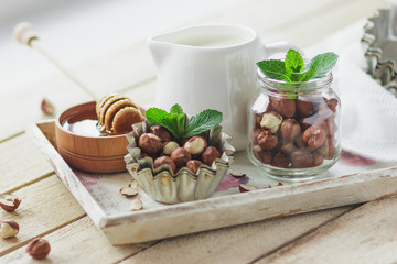 Honey in the wooden bowl, mint leaves, hazelnuts and jar with milk on the wooden tray
