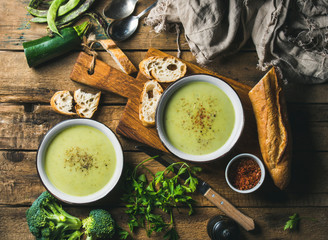 Two bowls of homemade pea, broccoli and zucchini cream soup served with fresh baguette and...